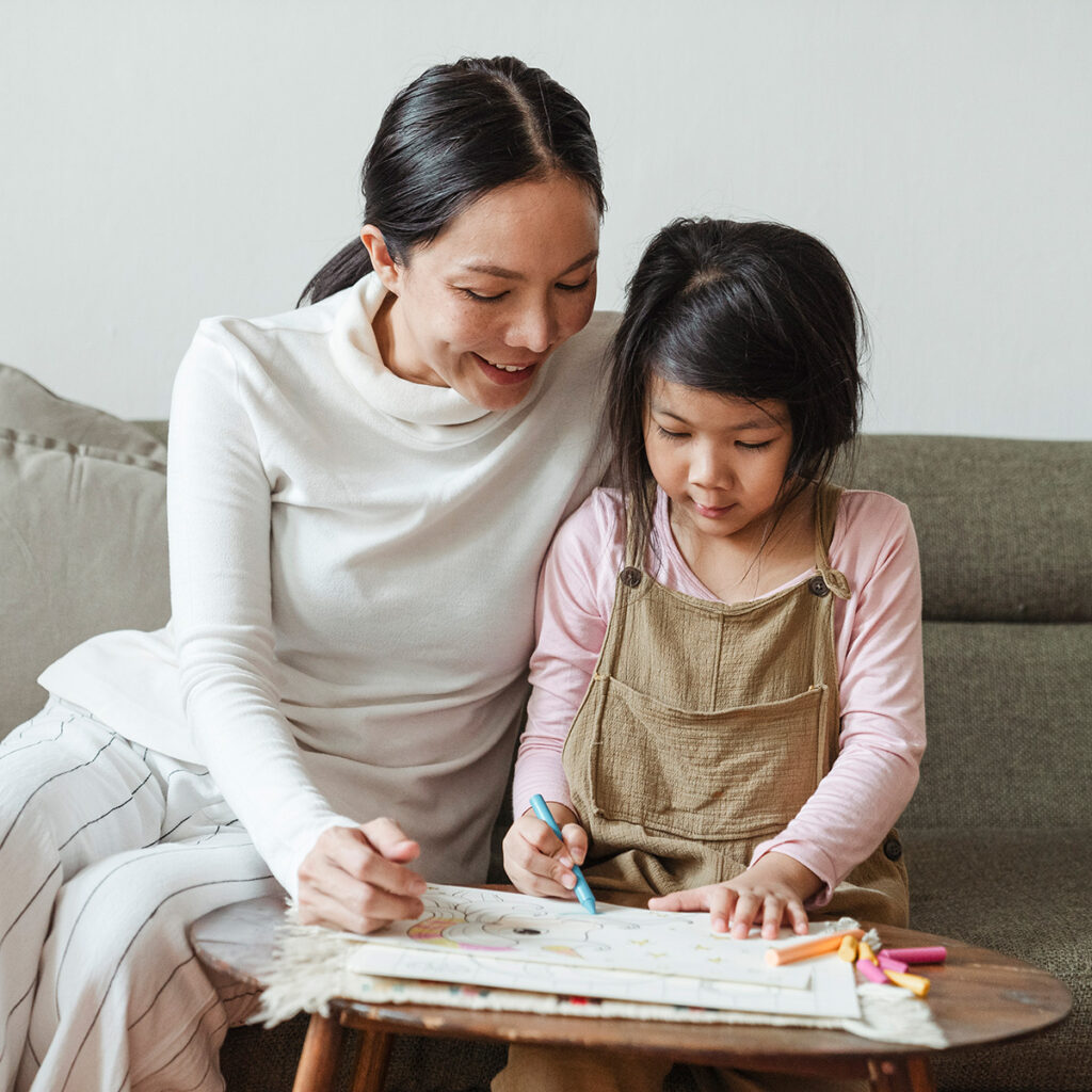 Asian mom and young daughter work on coloring art activity at home