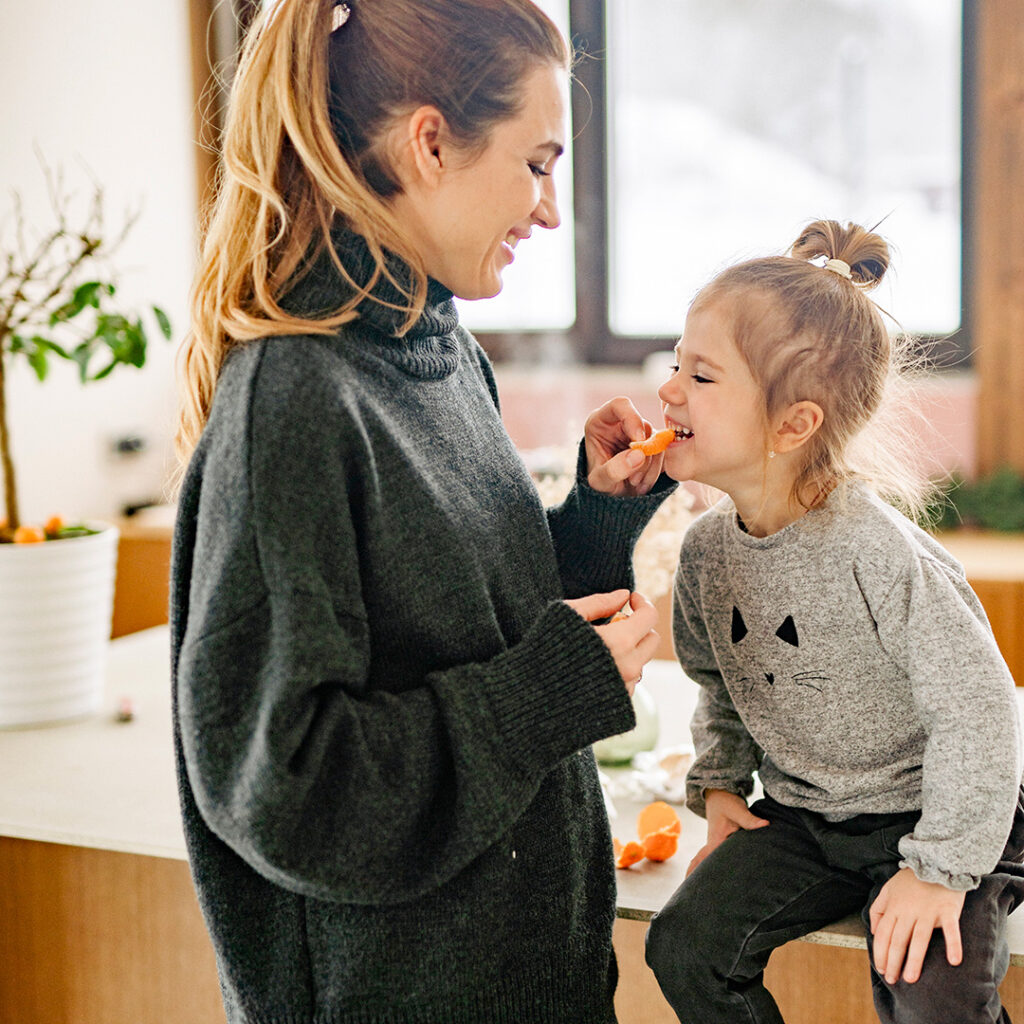 Young mom and daughter share clementine snack in a kitchen